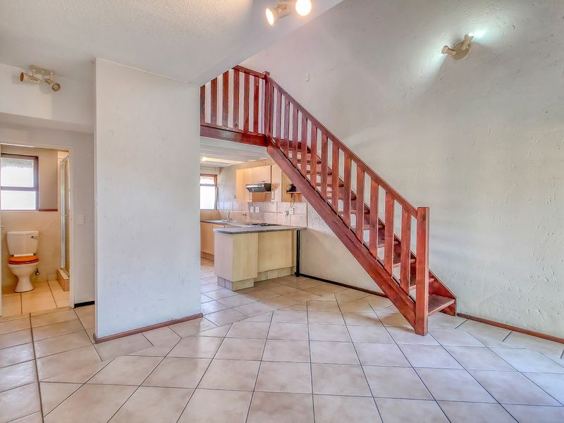 Open plan living area featuring a wooden staircase, tiled flooring, and an adjoining kitchen and bathroom in a functional, vacant apartment space.