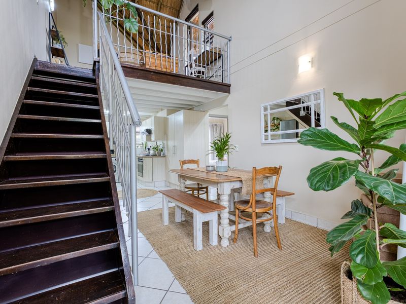 Open plan living area featuring a wooden staircase leading to a mezzanine level, tiled flooring, and neutral wall finishes.