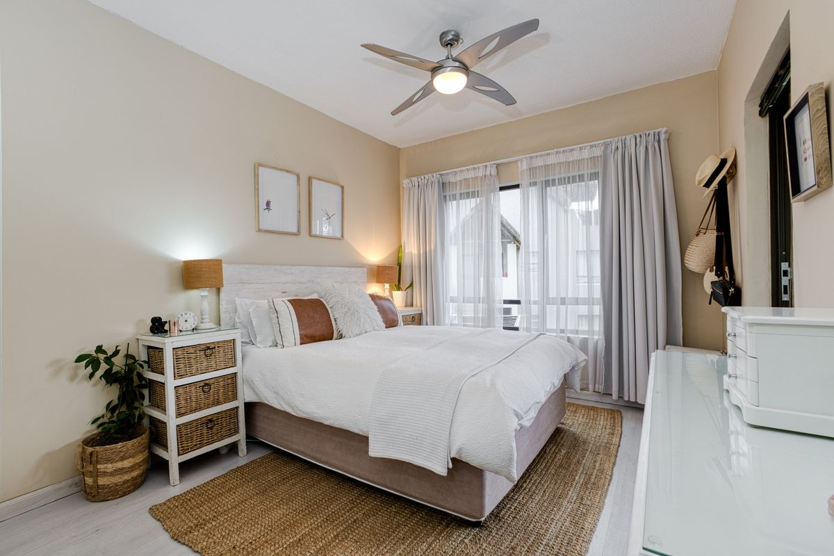 A well-maintained bedroom featuring a ceiling fan, neutral wall tones, and a sliding glass door providing natural light.