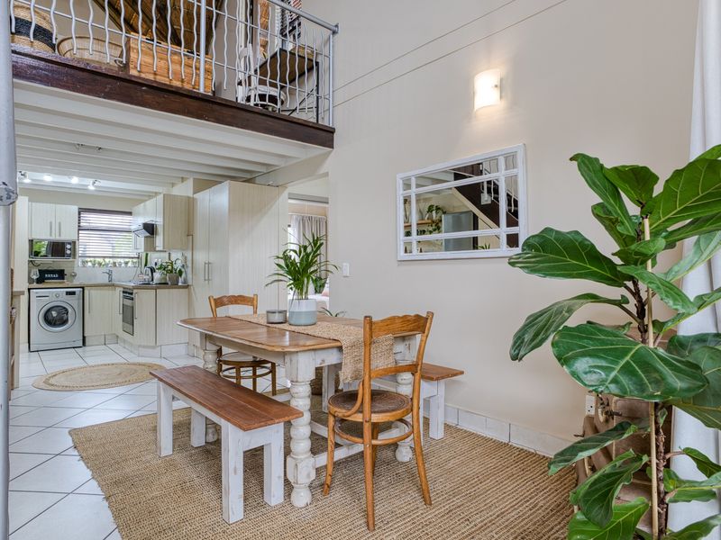 Open-plan living and dining area featuring a mezzanine level, exposed ceiling beams, and a functional kitchen with built-in cabinetry and appliances.