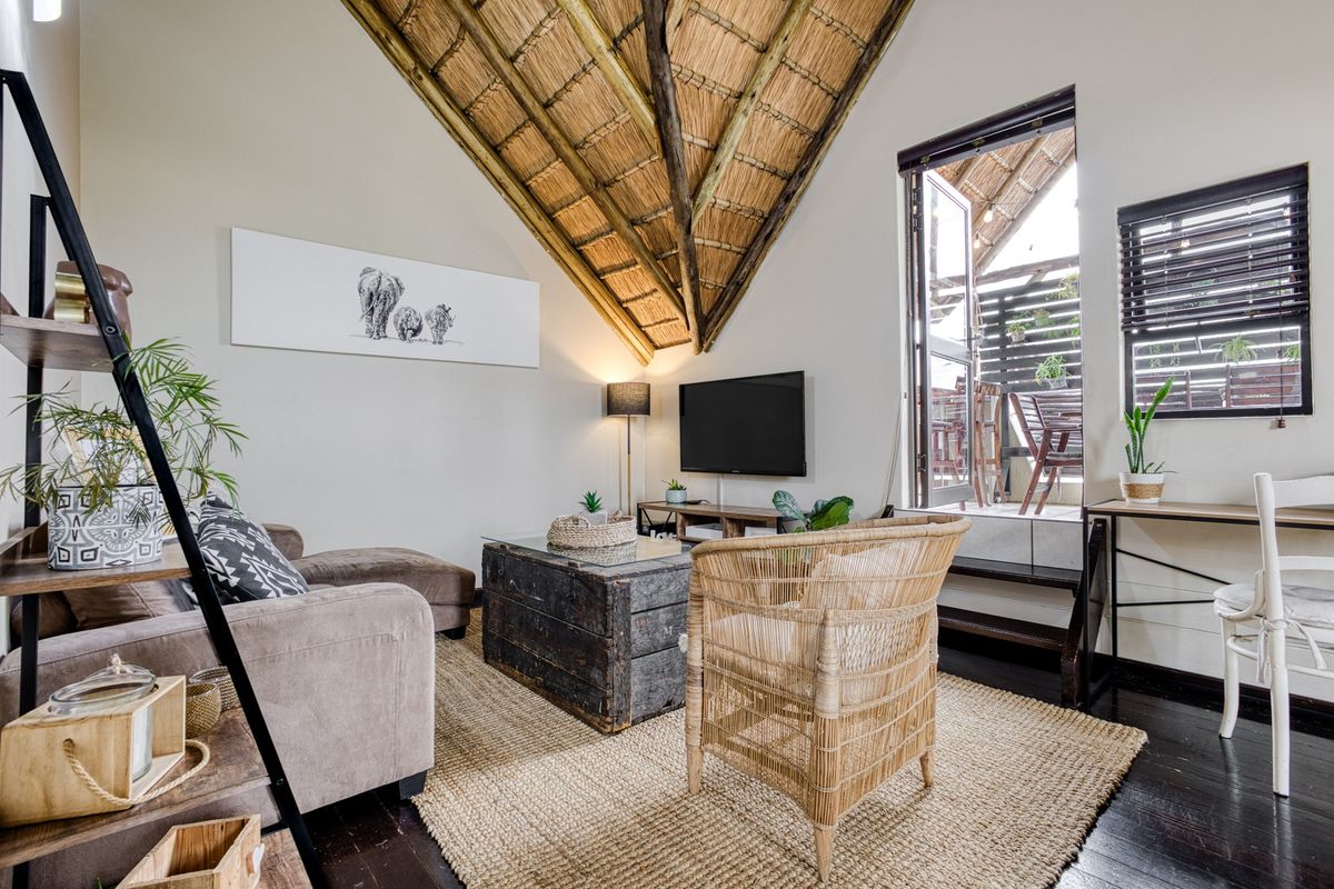 A cozy living room featuring a high exposed thatch ceiling with timber trusses, dark wood flooring, and direct access to a private balcony.