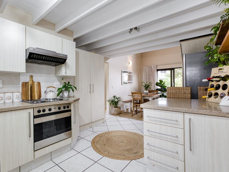 Open-plan kitchen and dining area featuring light wood-grain cabinetry, stone countertops, built-in oven and hob, and distinctive exposed beam ceilings.