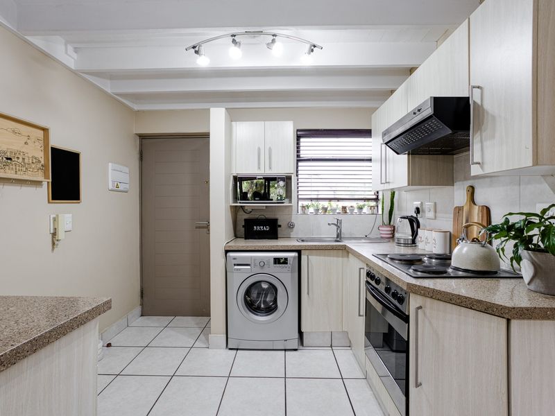 A functional kitchen featuring light wood cabinetry, granite countertops, tiled flooring, and integrated appliances including an oven, hob, and extractor fan.