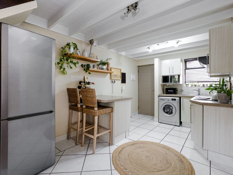 A functional kitchen featuring light-toned cabinetry, laminate countertops, integrated washing machine, built-in microwave, and a breakfast nook with tiled flooring and exposed beam ceilings.