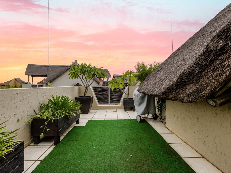 A private balcony featuring tiled flooring, an artificial grass section, and a unique thatched roof overhang, offering an open-air space for relaxation.