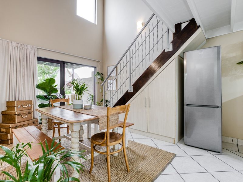 Open-plan dining area featuring double-volume ceilings, tiled flooring, and convenient under-stair storage cabinetry with access to a patio through sliding glass doors.