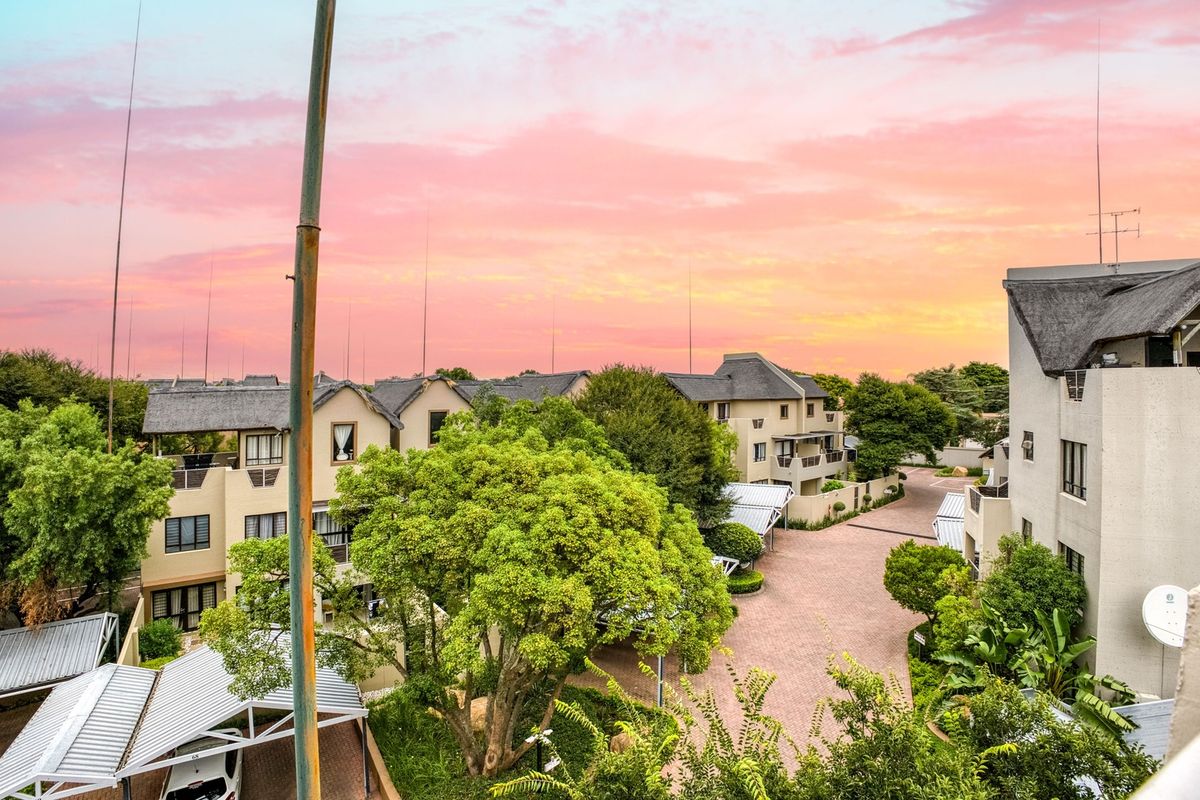 An elevated aerial view of a residential apartment complex featuring paved driveways, carports, and mature landscaping under a sunset sky.