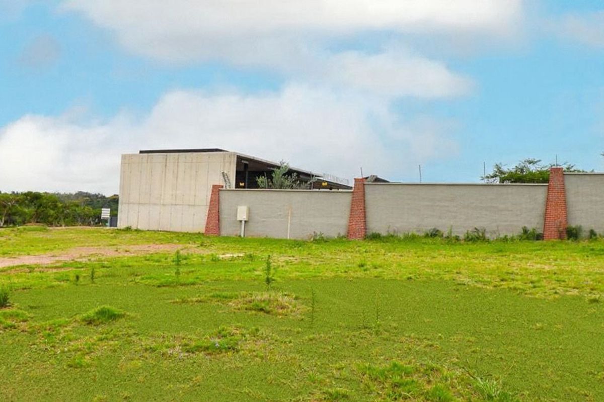 A view of a vacant residential plot featuring a modern concrete structure and a perimeter boundary wall with brick pillar accents.