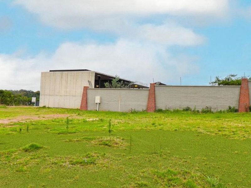 A view of a vacant residential plot featuring a modern concrete structure and a perimeter boundary wall with brick pillar accents.
