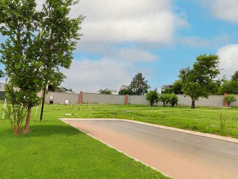 A view of a vacant residential plot featuring a paved driveway, established lawn, and a perimeter boundary wall.