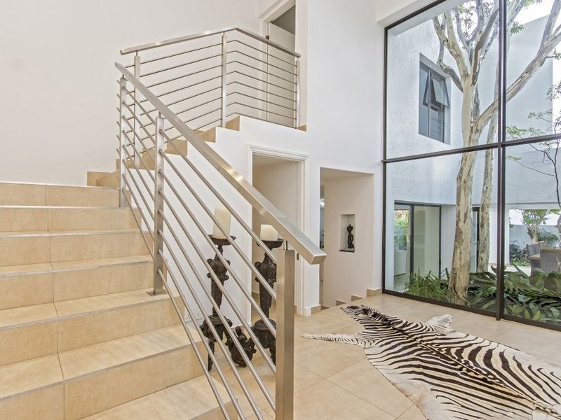 Spacious entrance hall featuring a modern tiled staircase with stainless steel railing and a large floor-to-ceiling window overlooking an internal courtyard.