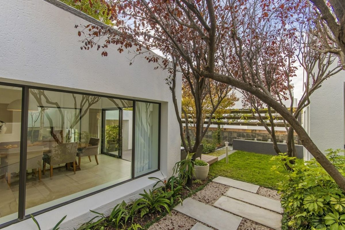 A well-maintained rear garden featuring a stone paver walkway, lush landscaping, and large sliding glass doors providing seamless indoor-outdoor flow.