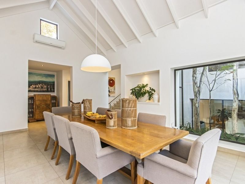 Spacious dining room featuring a high vaulted ceiling with exposed rafters, tiled flooring, and a large picture window overlooking a private courtyard.