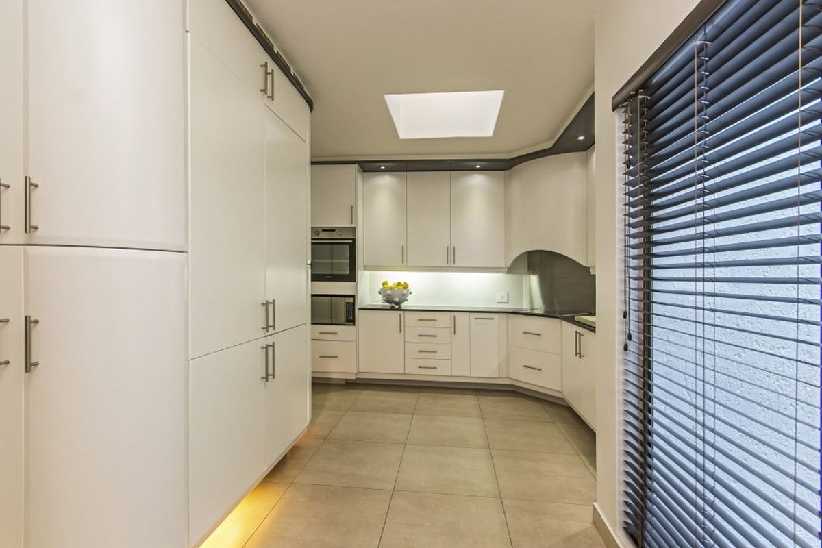 Modern kitchen featuring sleek white cabinetry, integrated appliances, stone countertops, tiled flooring, and a skylight providing ample natural light.