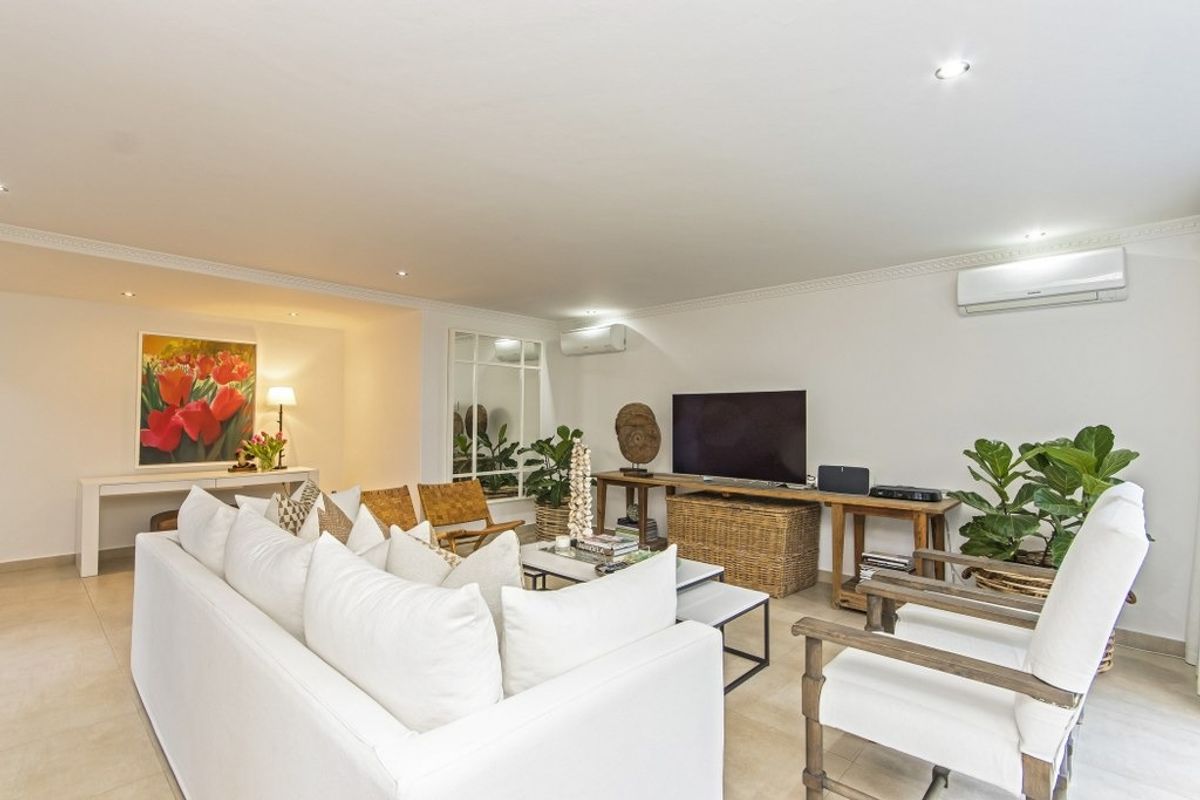A bright and spacious living room featuring tiled flooring, recessed downlighting, decorative ceiling cornices, and dual split-system air conditioning units.