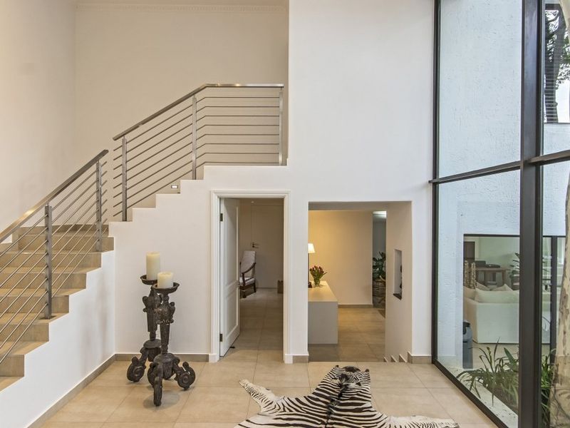 Spacious entrance hall featuring a modern staircase with stainless steel balustrades and expansive floor-to-ceiling windows providing natural light.