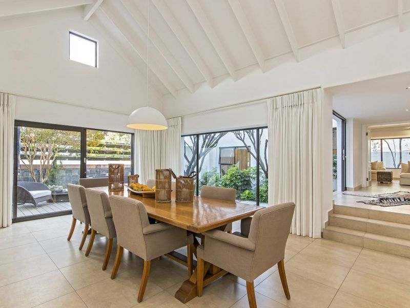 Spacious dining room featuring a vaulted ceiling with exposed rafters, large sliding glass doors, and neutral tiled flooring, offering a bright and airy atmosphere.