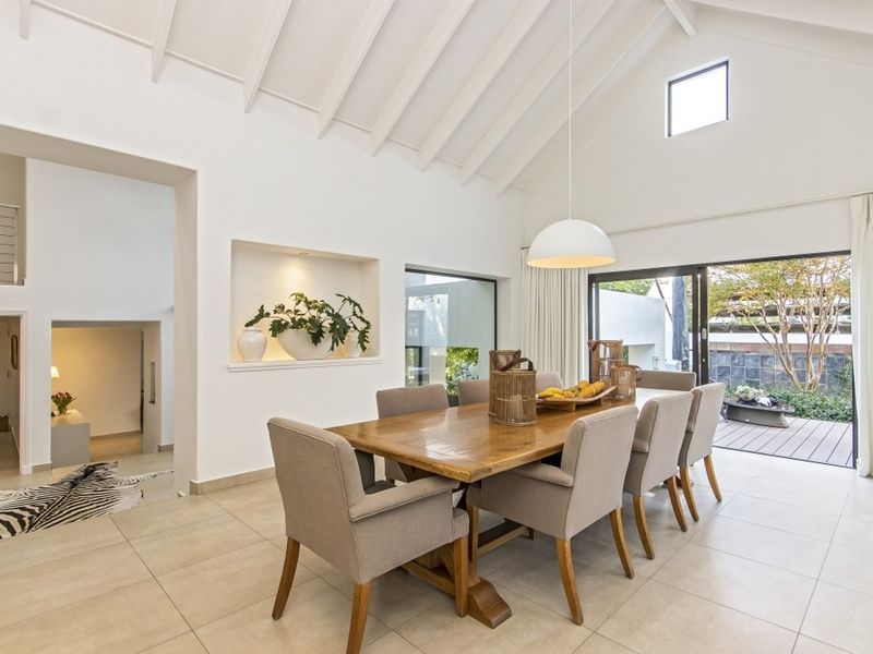 Spacious dining area featuring a high vaulted ceiling with exposed rafters, tiled flooring, and large sliding doors opening to an outdoor deck.