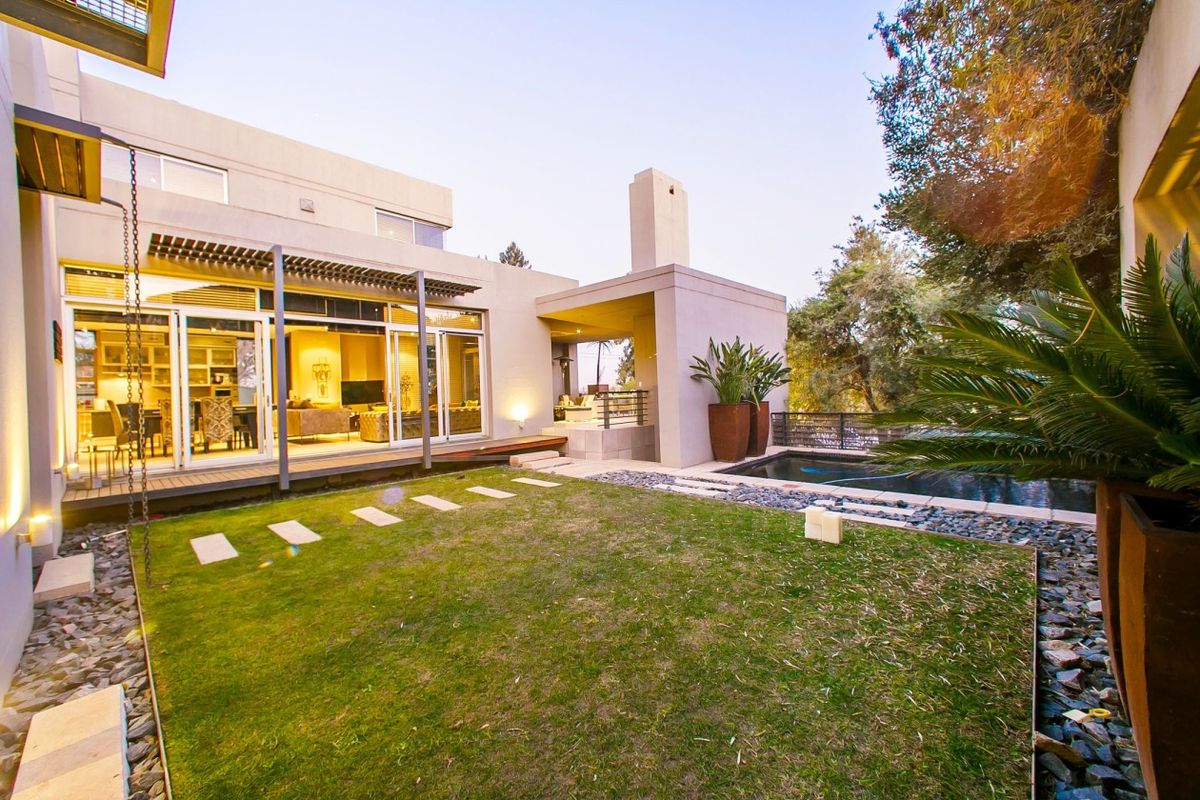 A modern rear exterior featuring a landscaped garden, timber decking, a swimming pool, and a covered patio with an integrated outdoor fireplace.