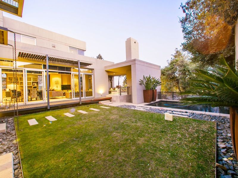 A modern rear exterior featuring a landscaped garden, timber decking, a swimming pool, and a covered patio with an integrated outdoor fireplace.