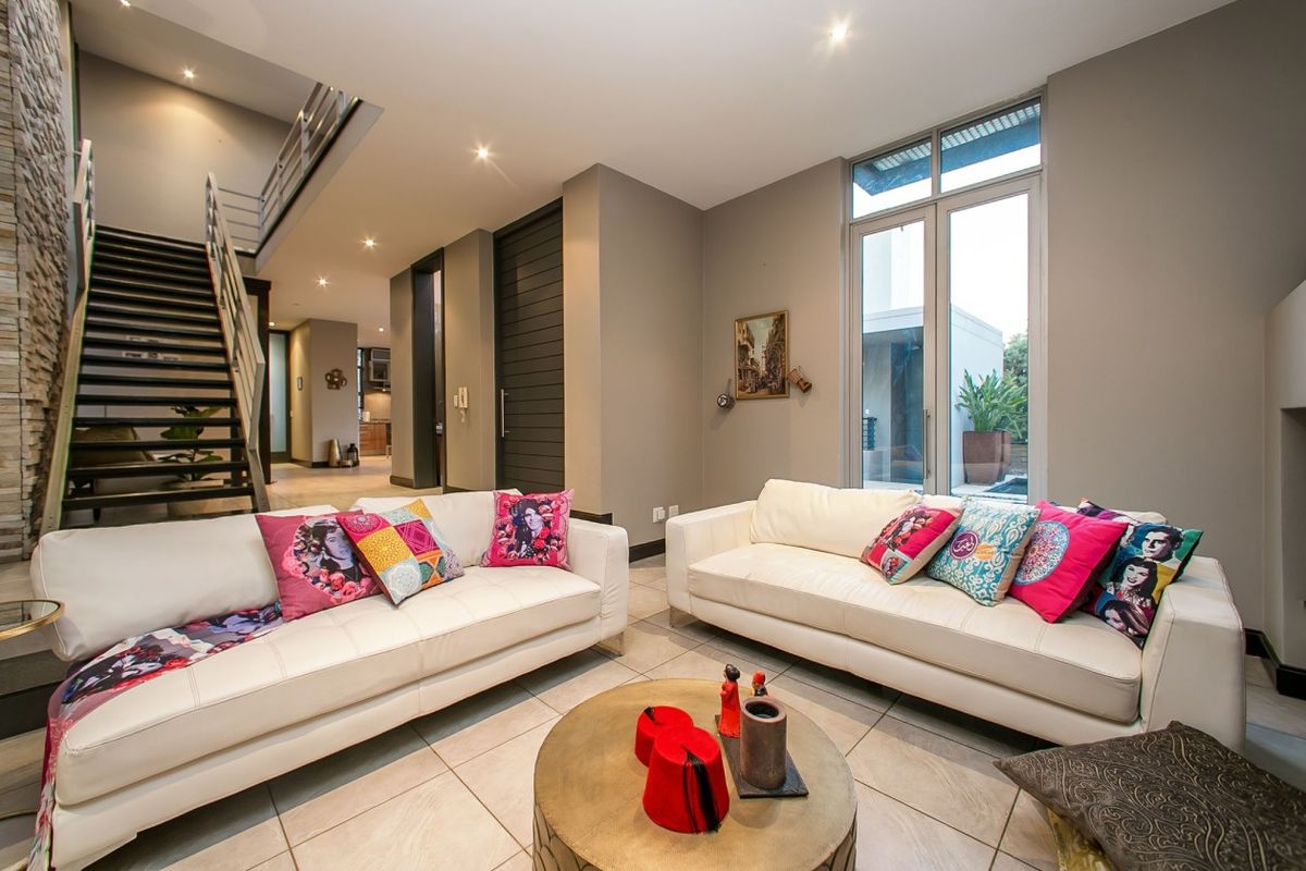 Spacious modern living room featuring tiled floors, a contemporary staircase, and large windows providing natural light and garden views.