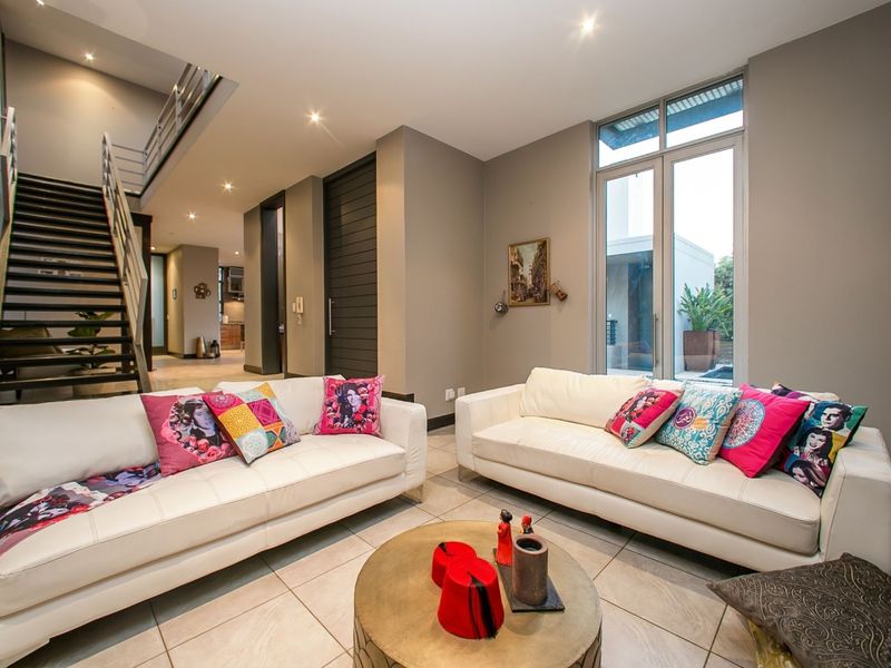 Spacious modern living room featuring tiled floors, a contemporary staircase, and large windows providing natural light and garden views.