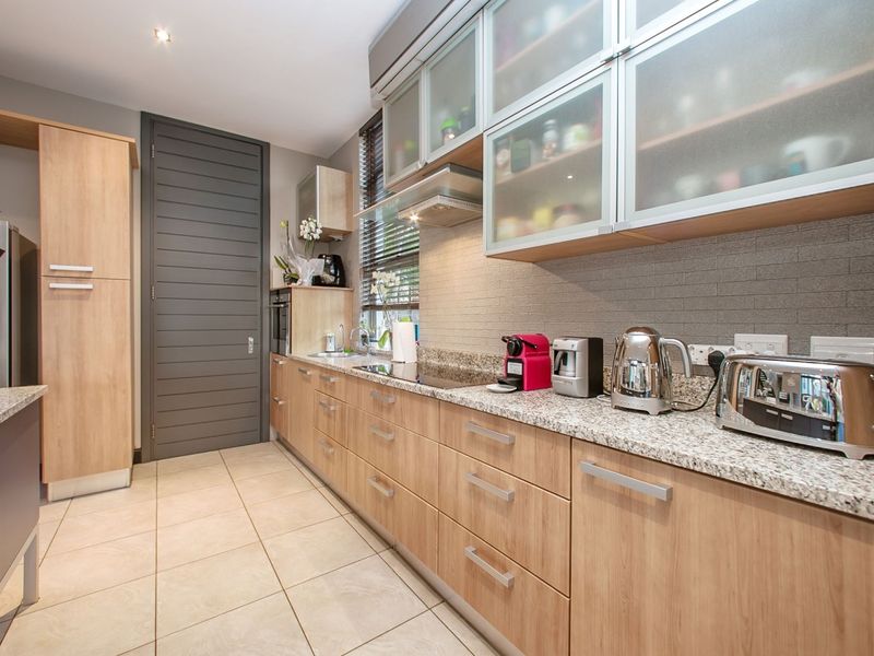 Modern kitchen featuring light wood cabinetry, granite countertops, frosted glass upper cabinets, and tiled flooring with integrated appliances.