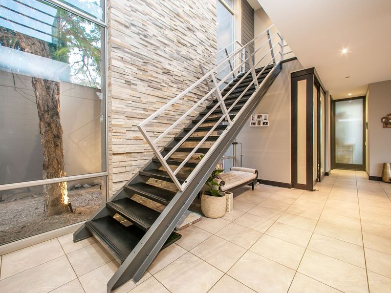 Modern entrance hallway featuring a striking metal staircase, stone feature wall, and expansive floor-to-ceiling windows overlooking a private courtyard.