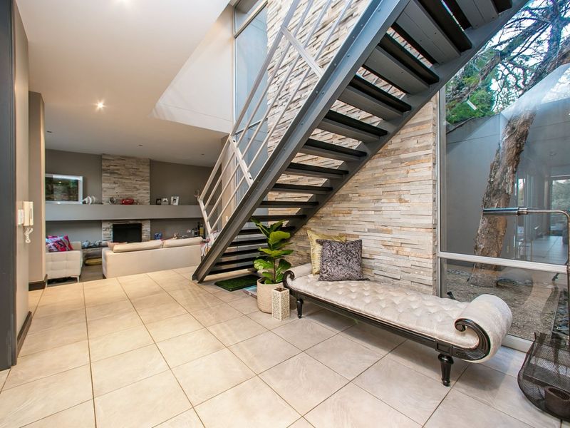 Modern open-plan living area featuring a striking open-tread metal staircase, stone feature wall, built-in fireplace, and expansive windows overlooking the garden.