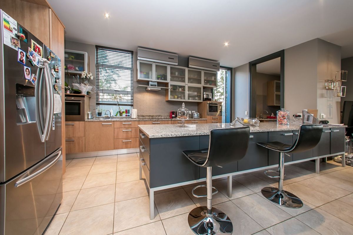 Modern kitchen featuring a central island with granite countertops, ample cabinetry, built-in appliances, and tiled flooring, offering a functional and contemporary cooking space.