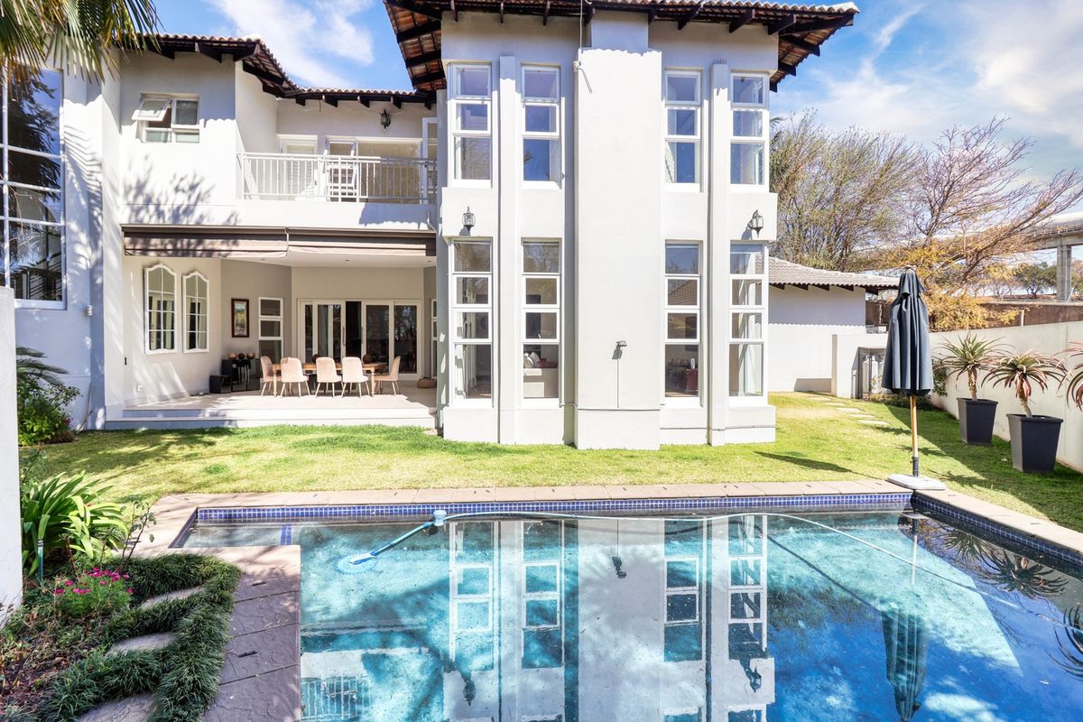 Rear view of the property featuring a swimming pool, covered patio area, upper balcony, and well-maintained garden space.