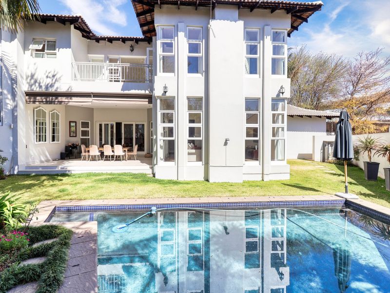 Rear view of the property featuring a swimming pool, covered patio area, upper balcony, and well-maintained garden space.