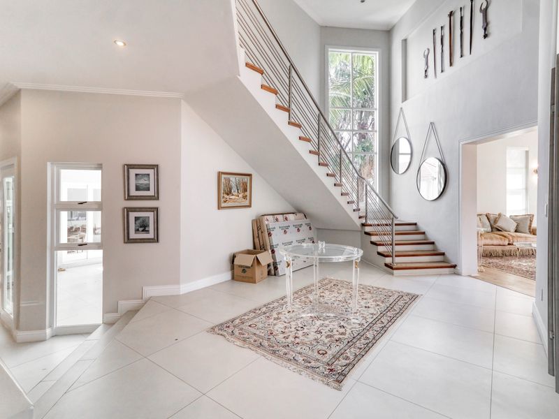 Spacious double-volume entrance hall featuring a modern staircase with metal balustrades, large windows, and neutral tiled flooring.