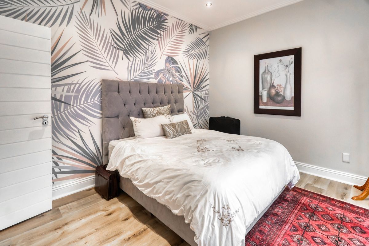 A well-maintained bedroom featuring laminate flooring, recessed downlighting, and a decorative feature wall with palm leaf wallpaper.