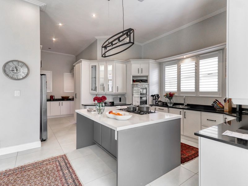 Modern kitchen featuring a central island with quartz countertops, shaker-style cabinetry, built-in oven, gas hob, and elegant plantation shutters.
