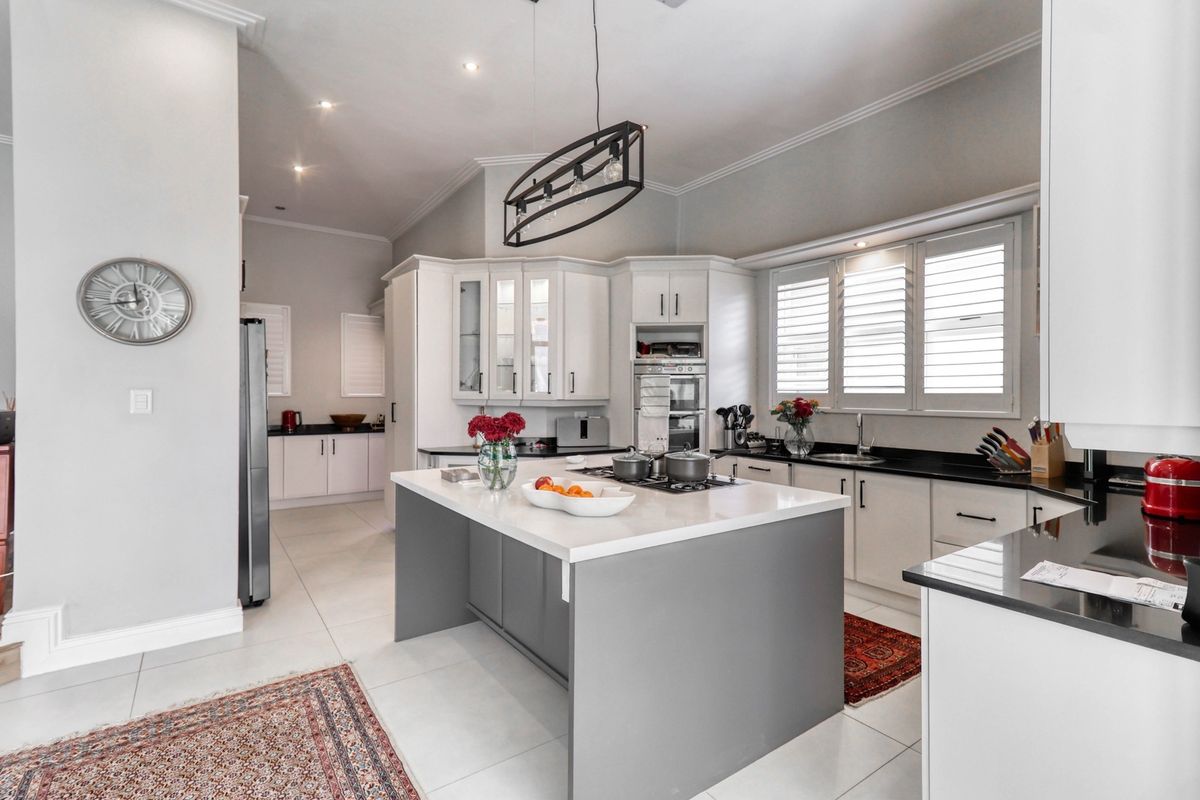 Modern kitchen featuring a central island with quartz countertops, shaker-style cabinetry, built-in oven, gas hob, and elegant plantation shutters.