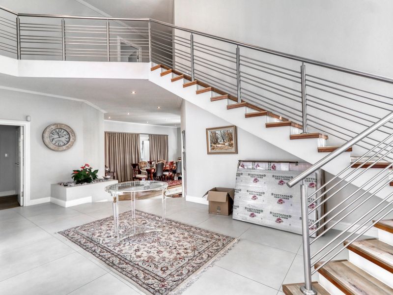 Spacious entrance hall featuring a modern staircase with stainless steel railings, wooden treads, and large format floor tiles leading into the open plan living area.