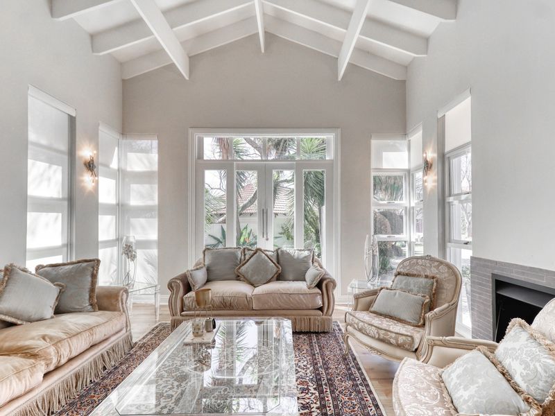 Elegant living room featuring a high vaulted ceiling with exposed beams, a fireplace, and large windows providing abundant natural light and garden views.