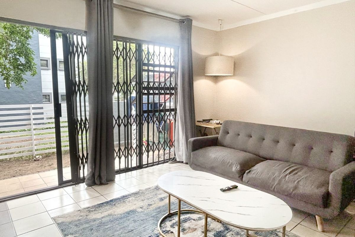 A bright living room featuring tiled flooring and a sliding glass door with a security gate leading to an outdoor area.