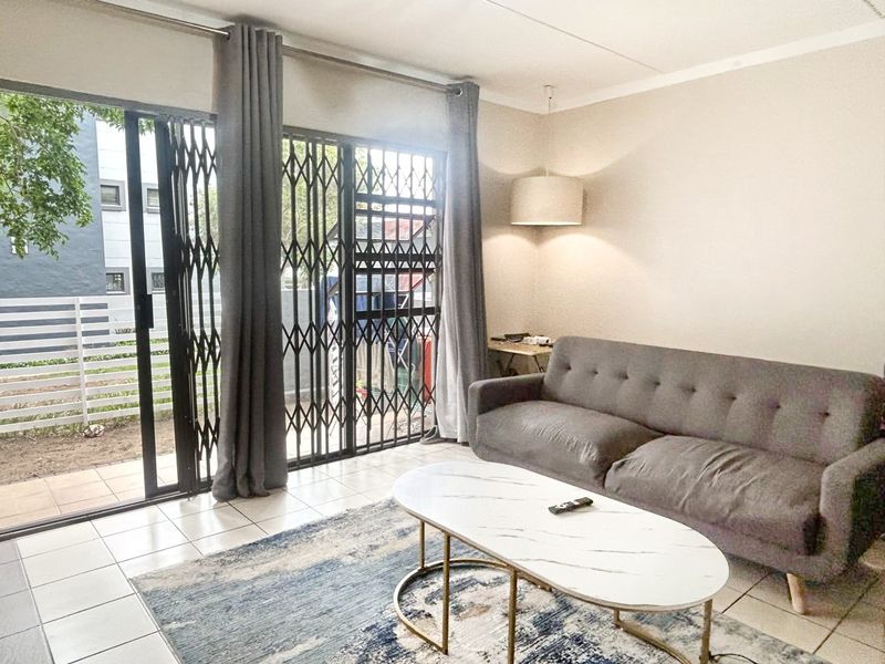A bright living room featuring tiled flooring and a sliding glass door with a security gate leading to an outdoor area.