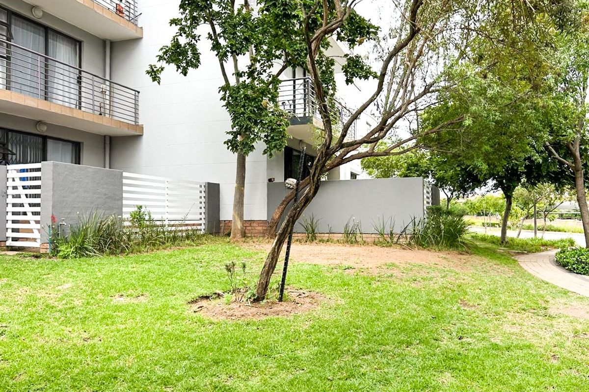 A view of the apartment building's rear exterior, featuring a landscaped garden, paved walkway, and private balconies with metal railings.