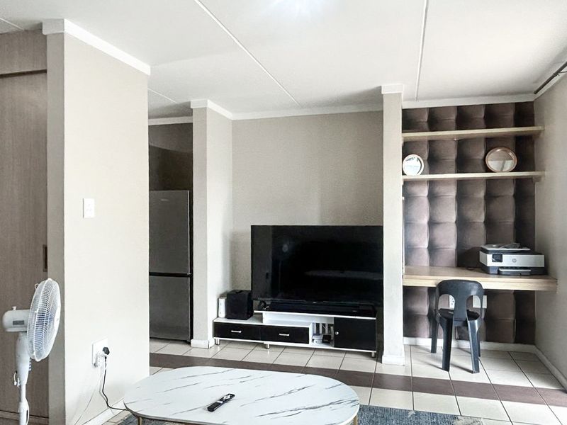 A living area featuring tiled flooring, a built-in desk with shelving, and decorative upholstered wall paneling.