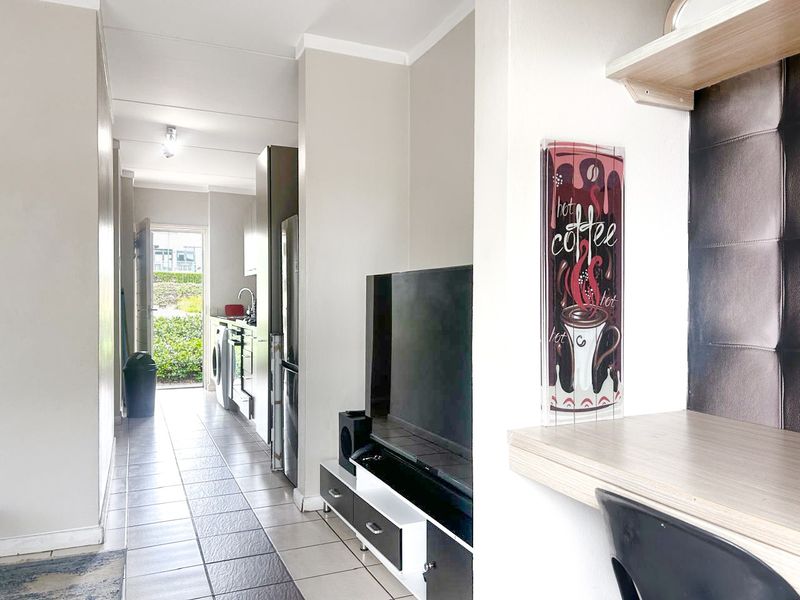 Open plan living area featuring tiled flooring, a built-in desk space, and a functional kitchen with integrated appliances leading to an exterior entrance.