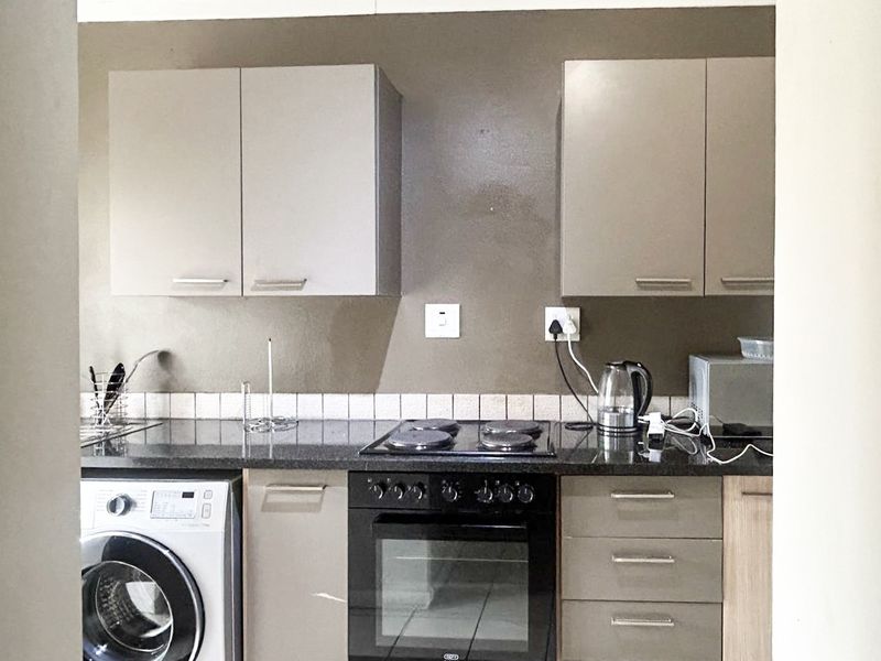 Compact kitchen featuring built-in cabinetry, granite countertops, an electric hob, oven, and integrated washing machine with a tiled backsplash.