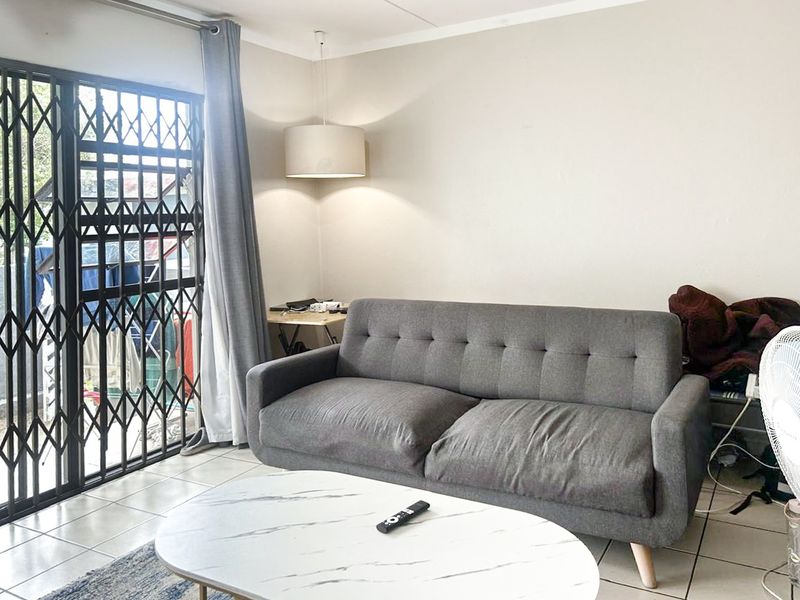 A living room featuring tiled flooring, a pendant light, and a sliding door with a security gate leading to an outdoor area.
