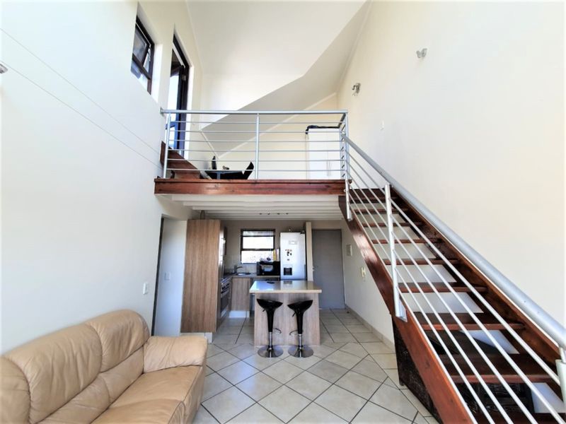 Open-plan living area featuring a timber staircase with stainless steel balustrade, a mezzanine level, and a functional kitchen with a central island.