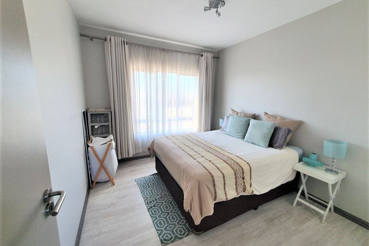 A well-maintained bedroom featuring light-toned laminate flooring, neutral wall finishes, and large windows with installed curtain tracks.