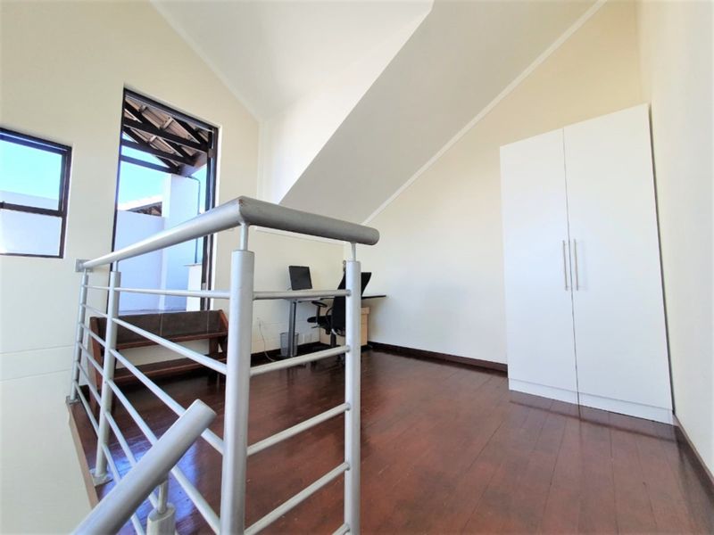 A bright loft-style office space featuring timber flooring, a vaulted ceiling, and a built-in wardrobe, with access to an outdoor balcony area.