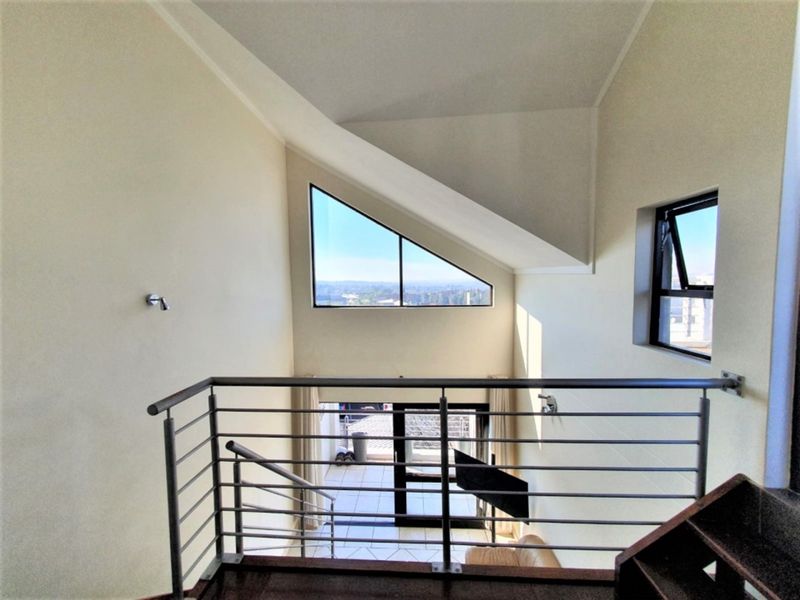 A bright, open-plan landing area featuring a modern stainless steel balustrade, a unique triangular window, and views overlooking the lower level.