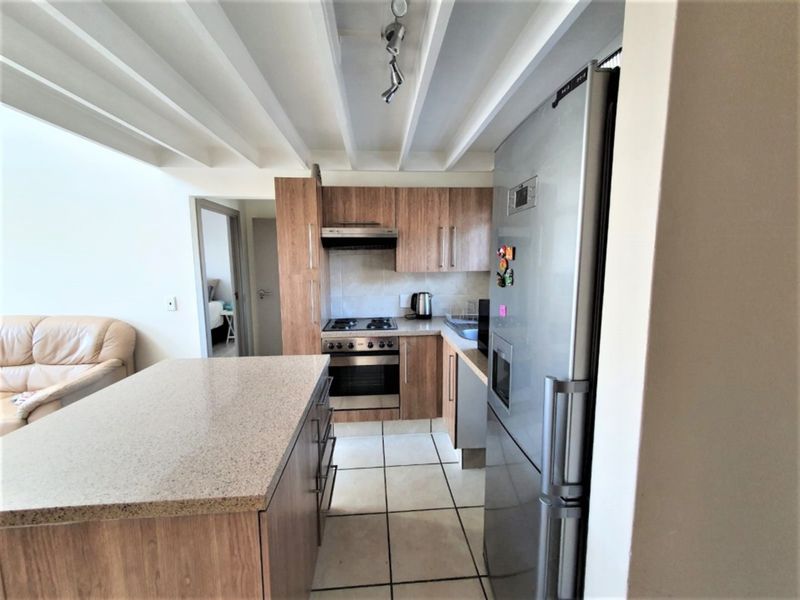 A functional kitchen featuring wood-finish cabinetry, stone countertops, a central island, and tiled flooring, complemented by exposed ceiling beams.